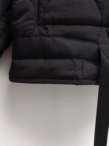 Close-up of black quilted puffer jacket detail featuring woven ribbon and stitching