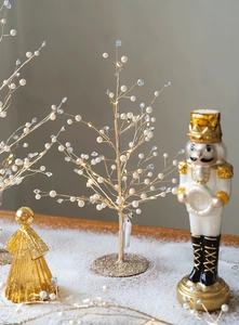 Macro view of golden LED tree with white pearls and crystals on snowy surface