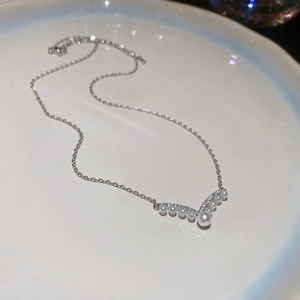 Macro shot of silver V-shaped pearl necklace with zircon accents on a white plate
