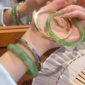 Close-up of stacked resin emerald green bangles paired with gold and silver metal rings