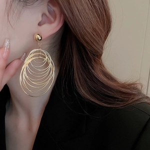 Close-up of a model wearing tiered golden circular drop earrings with a metallic finish