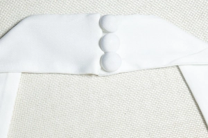 Détail d'une robe en tricot blanc montrant trois boutons recouverts de tissu sur le côté
