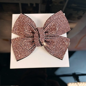 Detail of pink rhinestone bow hair clip with sparkling crystal inlay on white stand