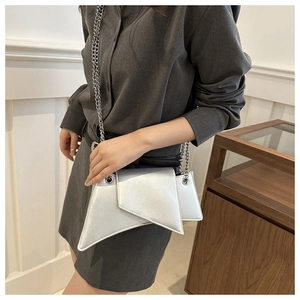 Detail of silver geometric square bag with metal chain strap worn by a model