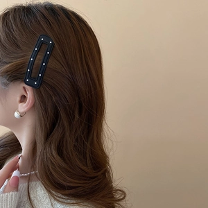 Close-up of model wearing a black matte hair clip with white polka dots and pearl earring