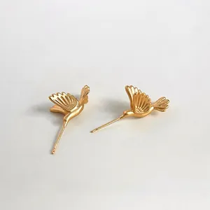 Macro shot of matte gold hummingbird stud earrings featuring elegant brushed metal texture