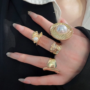 Detail view of gold ring set with pearls and textured irregular metal designs on finger