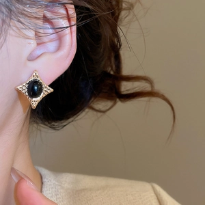 Close-up of vintage gold star stud earring with black oval stone and sparkling crystals