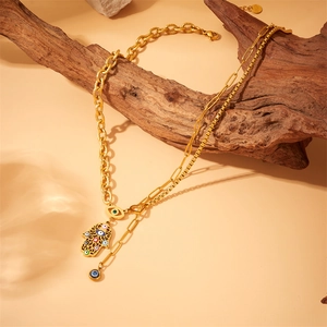 Double-layered gold evil eye necklace with Hamsa hand charm on a rustic wood display