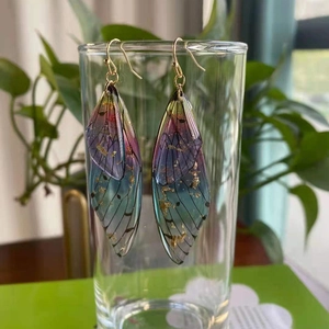 Detailed shot of gradient wing earrings with gold foil hanging on a clear glass rim