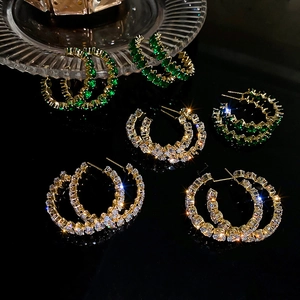 Close-up of golden hoop earrings featuring green and white cubic zirconia stones