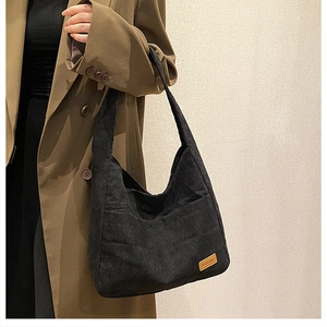 Detail of black corduroy tote bag texture with small brand label and soft fabric ridges