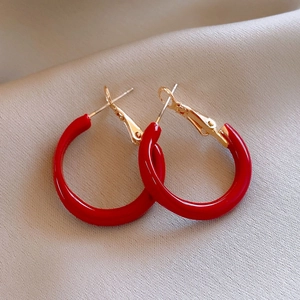 Detailed close-up of glossy red round hoop earrings with gold metal posts on silk cloth