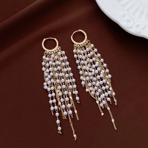 Close-up of elegant gold tassel earrings with white pearls on dark velvet background