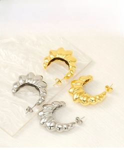 Macro shot of gold and silver chunky croissant twisted hoop earrings on textured surface