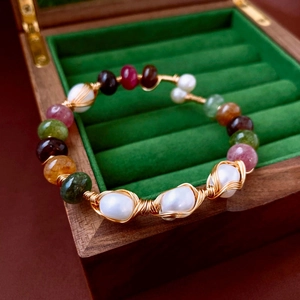 Detailed view of handmade multi-gemstone and pearl wire-wrapped bracelet on velvet box