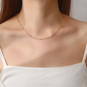 Detail of 18K gold plated beaded snake chain necklace worn on a woman neck
