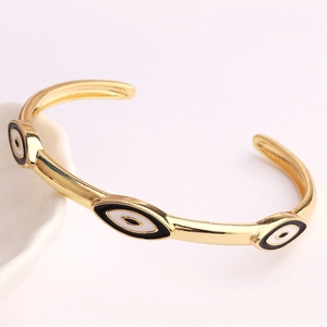 Detail of gold evil eye cuff bracelet with enamel drip oil pattern on white ceramic