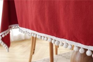 Detail of red cotton tablecloth with soft white pom pom fringe and woven texture