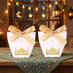 Close-up of white Eid gift boxes with gold mosque patterns and silk ribbons
