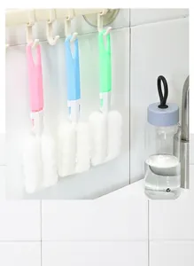 Three colorful sponge bottle brushes with long handles hanging on kitchen wall hooks