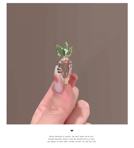 Close-up of a carrot brooch with pink crystal and golden setting worn on hand