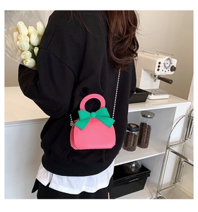 Close-up of a pink mini crossbody bag with a green bow on a model in a cafe