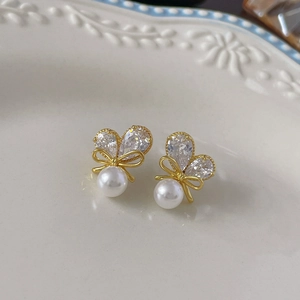 Detailed close-up of zircon bowknot earrings with white pearls on a ceramic plate