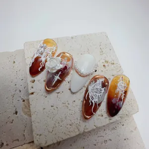 Detailed view of amber almond nails with embossed roses, pearls and rhinestones decoration