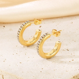 Macro detail of gold C-shaped earrings with shimmering rhinestones on textured stone