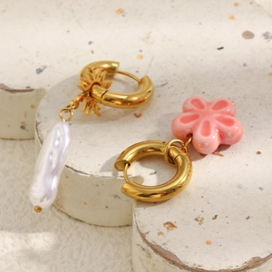 Macro shot of asymmetric gold flower and pearl earrings on textured stone surface