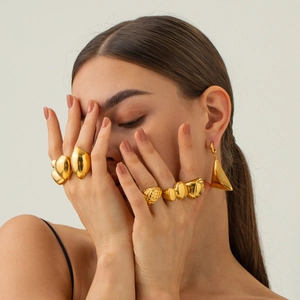 Primo piano di una modella con diversi anelli e orecchini in acciaio placcati oro 18 carati