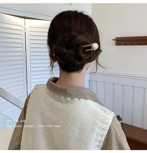 Detail showing a gold U-shaped hairpin with a large pearl in an elegant bun hairstyle