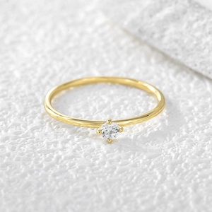 Minimalist gold plated four-prong solitaire zircon ring on a white textured stone base