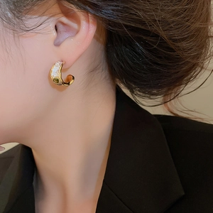 On-ear detail of C-shaped gold pearl earrings with white enamel and green zircon accents