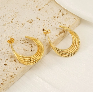 Detail of layered gold-plated U-shaped earrings with fine textured lines on marble