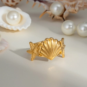 Vue détaillée d'une bague dorée coquillage et étoile de mer sur sable et perles