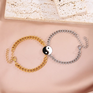 Close-up of gold and silver couple bracelets with Yin Yang charms on silk background