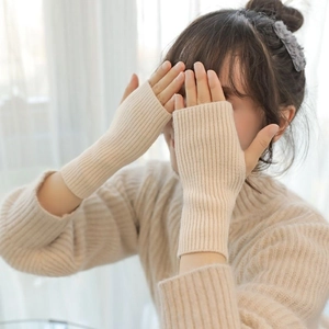 Close-up of beige knitted fingerless gloves worn by a model in soft natural window light