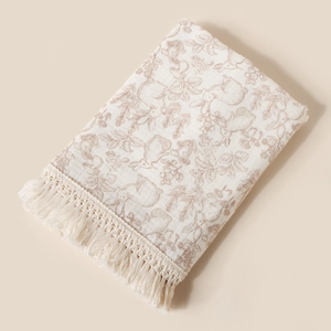 Detailed view of cream cotton gauze baby blanket with rabbit print and tassels