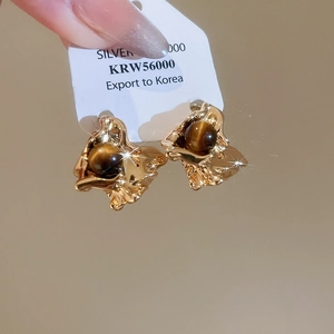 Macro shot of gold-plated lava texture earrings with tiger eye stone and silver pins