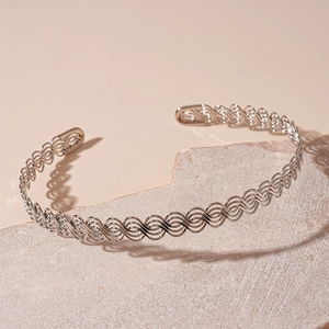 Close-up of silver open cuff bracelet with intricate woven texture on a stone pedestal