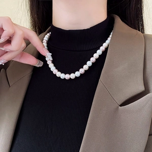 Detail view of round white and pink pearls on a model wearing a brown blazer