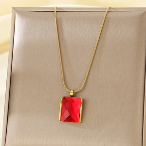 Detailed close-up of a gold snake chain necklace with a faceted red rectangular gemstone