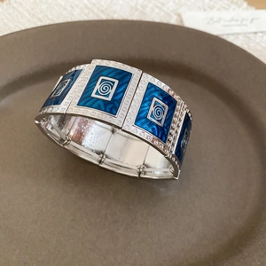 Detail of blue enamel geometric patterns on a silver wide elastic bracelet