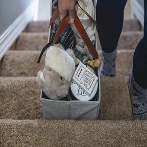 Close-up of a grey fabric stair basket with leather handles being carried on the stairs