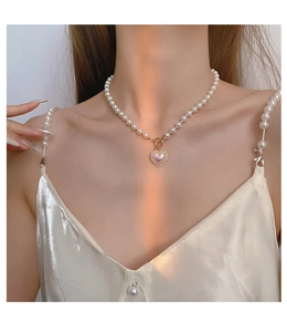 Detail of a pearl heart necklace on a model wearing a silk dress with pearl straps