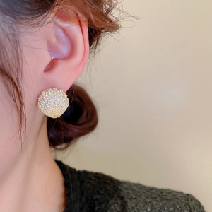Macro shot of gold shell earrings with pavé crystals on ear lobe for elegant look