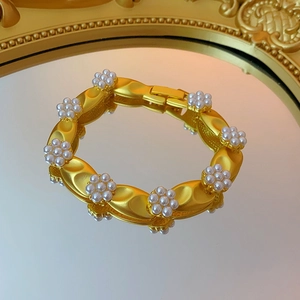 Detail of a vintage golden bracelet with white pearl flowers on a decorative mirror surface