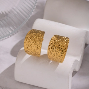 Détail de larges boucles d'oreilles dorées en C avec texture de lave sur pierre blanche